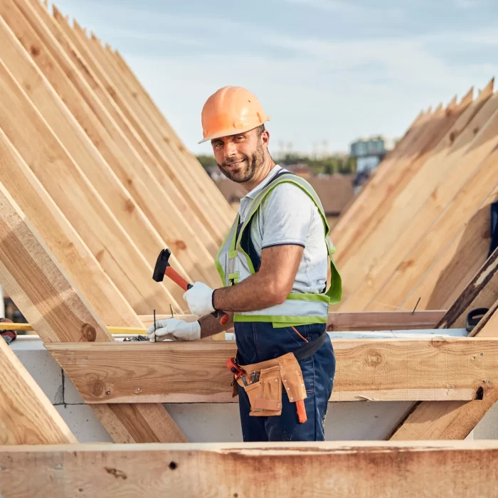 A builder smiling while hammering a nail on the upside down roof wooden frame. A builder smiling while hammering a nail on the upside down roof wooden frame.